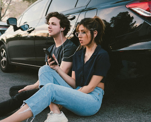 A man sitting down with a friend listening to music.
